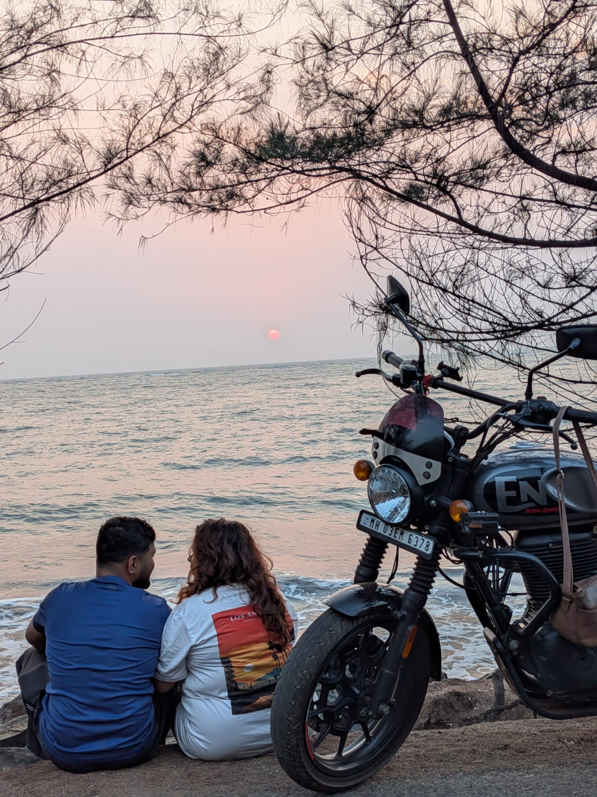 Tejas and Varsha sitting by the sea at sunset with their bike